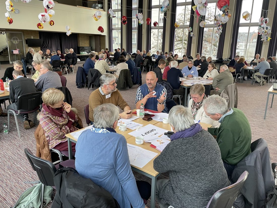 Mensen in gesprek aan tafels tijdens een synodale bijeenkomst